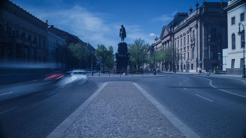 Road by buildings in city against sky