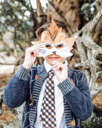 Portrait of boy holding maple leaf while standing in park during autumn