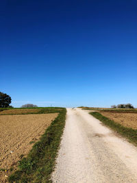 Road amidst field against clear blue sky