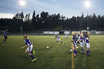 Girls playing soccer on field against sky