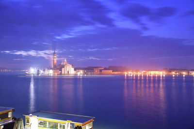 Illuminated buildings by sea against sky at night