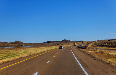 Road passing through landscape against clear blue sky