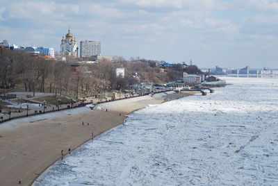 Scenic view of frozen river amidst buildings in city against sky