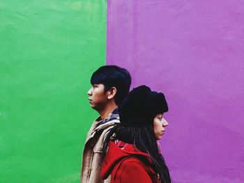 Side view of friends wearing warm clothing while standing by painted wall