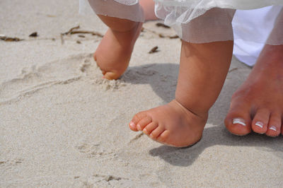 Low section of mother and baby walking on sand at beach 