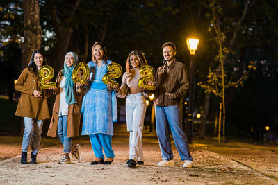 Cheerful friends holding balloon while standing outdoors