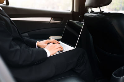 Midsection of businessman using laptop in car