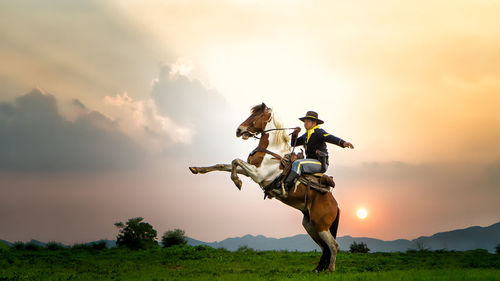 Mid adult man riding horse against sky during sunset