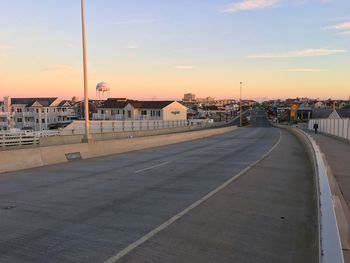 Road by buildings against sky during sunset