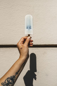 Cropped image of hand holding blueberry ice cream against wall