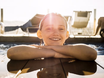 Portrait of smiling girl enjoying in swimming pool at resort against sky