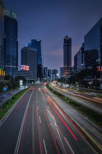 Light trails on city street by buildings against sky