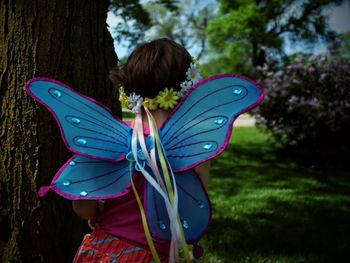 Rear view of girl wearing butterfly costume by tree trunk