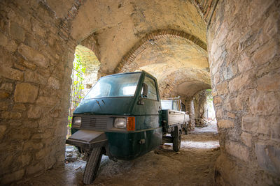 Unique three-wheeled vehicle parked in ancient stone ruins during daytime