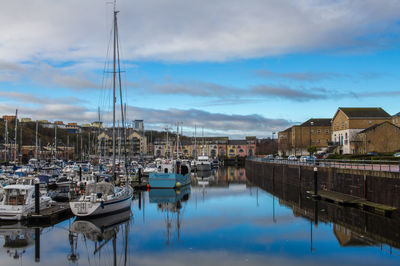 Boats moored at harbor against sky in city