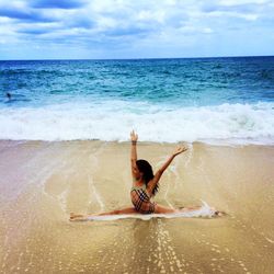 Young woman stretching on sea shore with arms raised