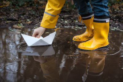 Low section of boy playing with paper boat on puddle during rainy season