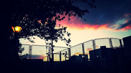 Low angle view of chainlink fence against sky at sunset