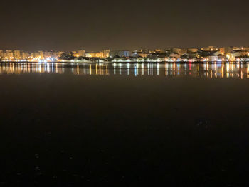 Illuminated buildings by sea against sky at night