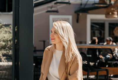 Woman in beige coat smiling outdoors, casual chic style