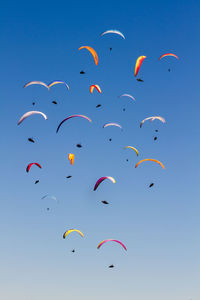 Low angle view of silhouette people paragliding against clear blue sky