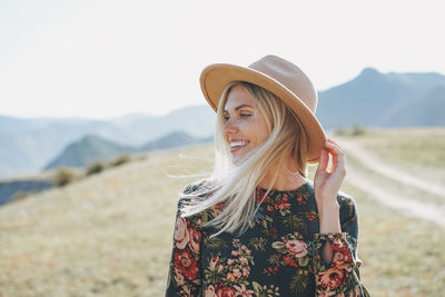 Beautiful smiling blone young woman traveler in dress and felt hat on road, trip to mountains, altai