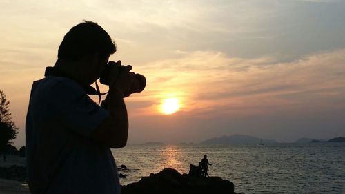 Silhouette man photographing sea against sky during sunset