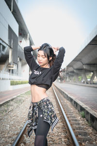 Beautiful young woman standing on railroad track against sky