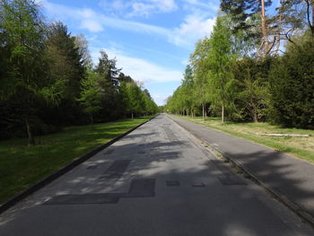 Empty road amidst trees against sky