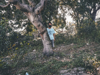 Man standing by tree trunk in forest