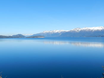 Scenic view of lake and snowcapped mountains against clear blue sky