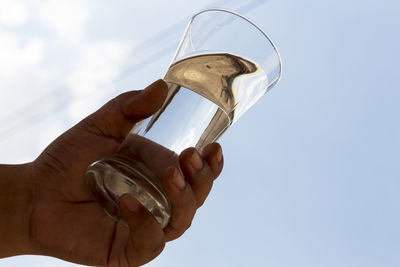 Cropped hand holding drinking glass against sky