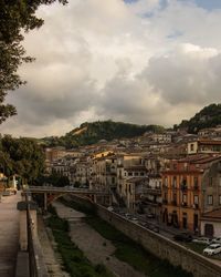 Arch bridge over stream in city against cloudy sky