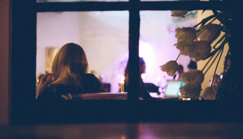 Woman sitting in cafe seen through glass window at night