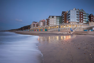 View of beach by buildings against blue sky