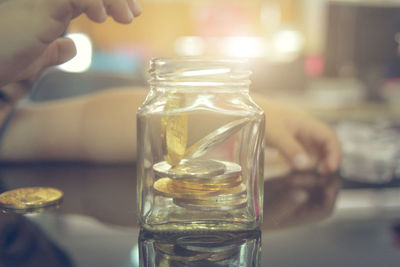 Close-up of hand by coins in glass jar on table