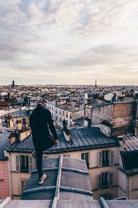 Rear view of man standing on roof against buildings in city