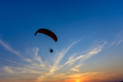 Low angle view of person paragliding against sky during sunset