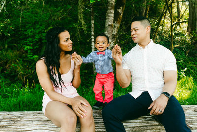 Straight on portrait of two parents holding hands with their baby