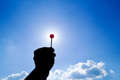 Cropped image of hand holding lollipop against blue sky