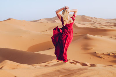 Young woman wearing red dress while standing at desert against clear sky