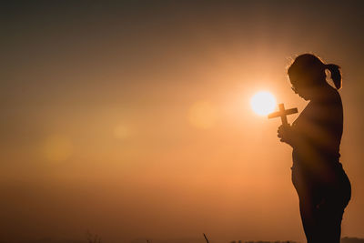 Silhouette woman standing against orange sky during sunset