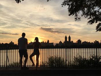 Rear view of friends standing by railing against reservoir at central park