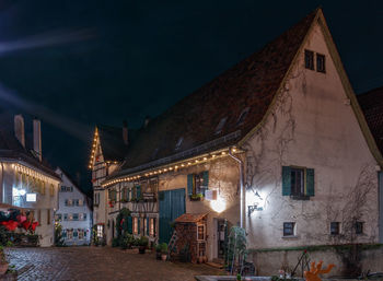 Illuminated street amidst buildings against sky at night