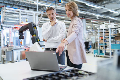 Businessman and businesswoman with laptop talking in a modern factory hall