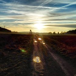 Road passing through field at sunset