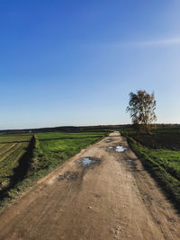 Dirt road amidst field against clear sky