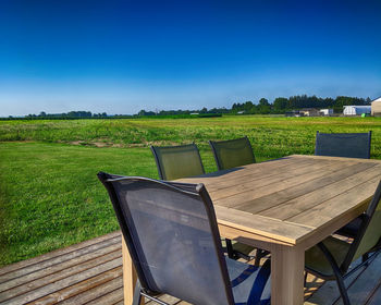 Empty chairs and table on field against blue sky