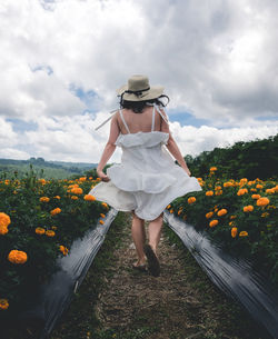 Rear view of woman standing on flowering plants against cloudy sky