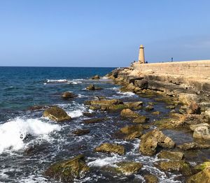 Lighthouse by sea against clear sky